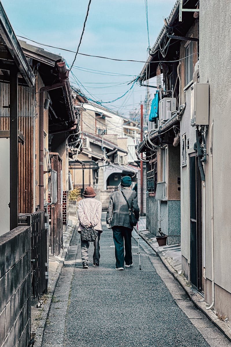 Elderly couple strolling down a narrow alley in a traditional Japanese neighborhood.