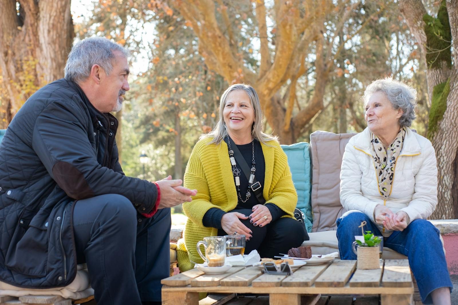 Three senior adults enjoying tea outdoors on a wooden table in Portugal's forest park.